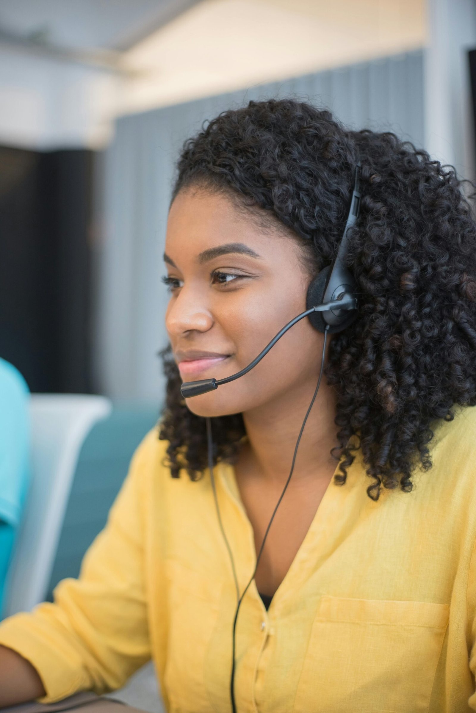 Focused call center agent with curly hair in a yellow blouse providing customer support.